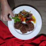 servirane pljeskavice iz rerne uz povrće i sos na belom tanjiru