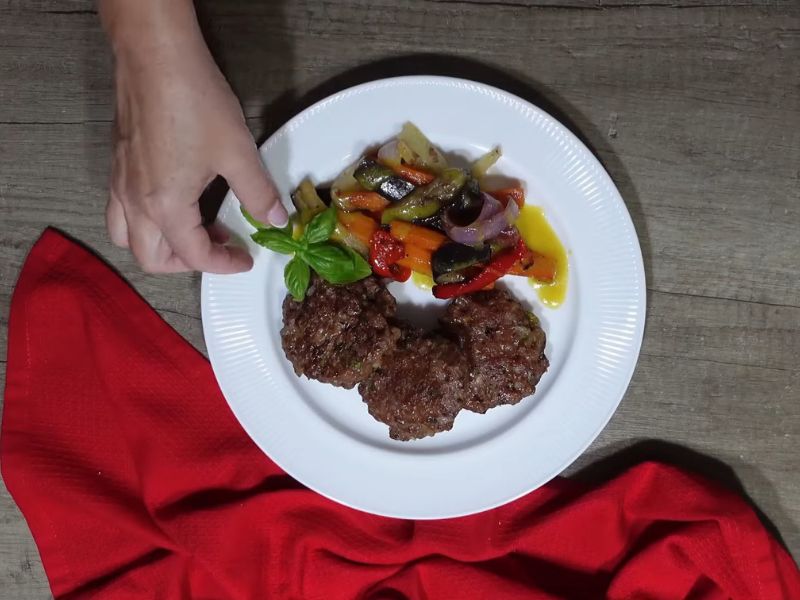 servirane pljeskavice iz rerne uz povrće i sos na belom tanjiru